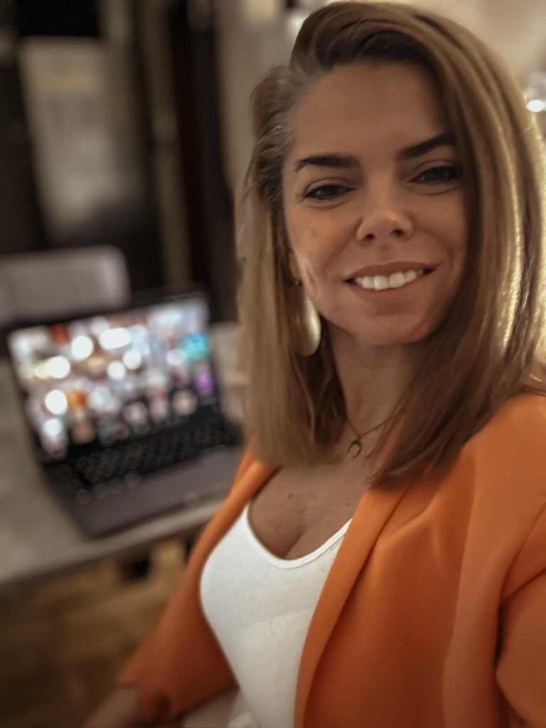 Mariane Michels lacht am Schreibtisch, hinter ihr läuft ein Zoom-Call auf dem Laptop